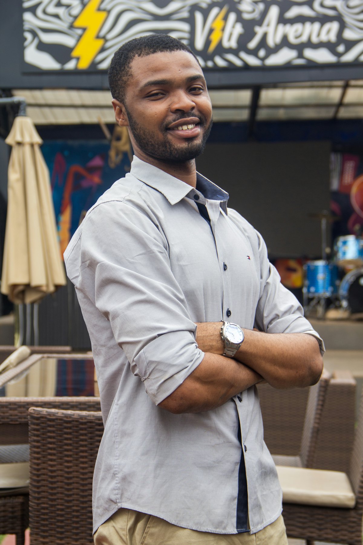 A smiling man in a grey shirt, arms folded, standing outside a venue in Nigeria