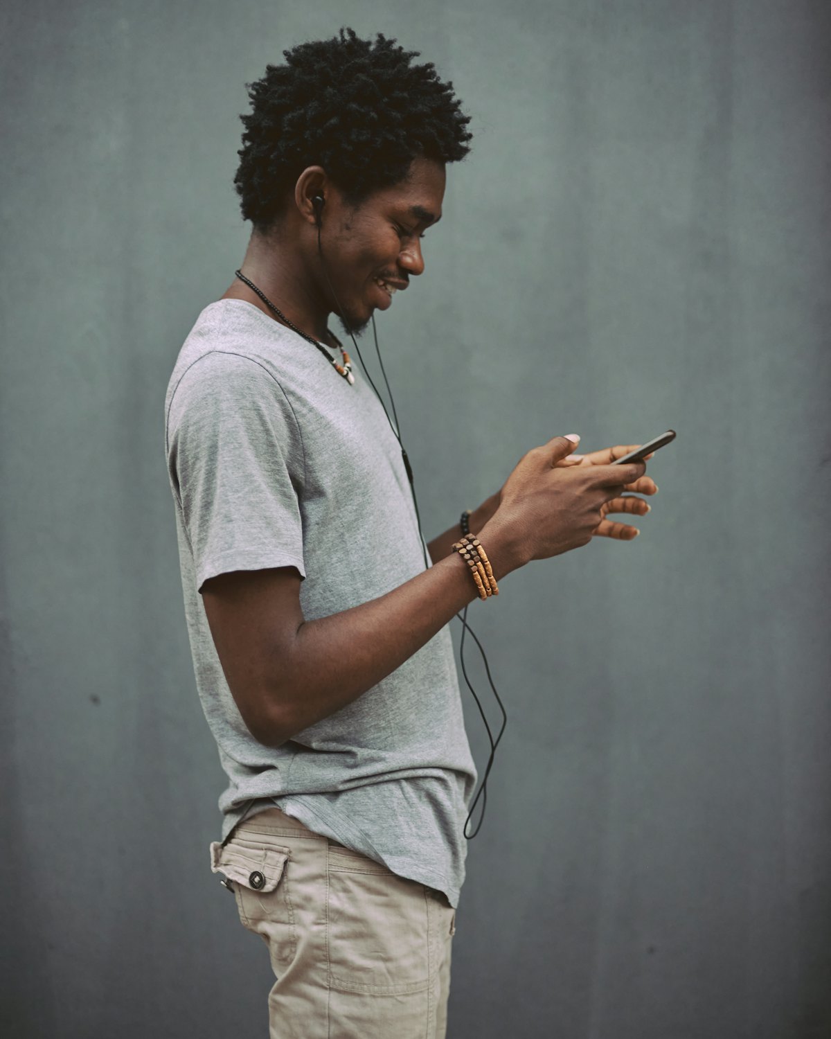 A young man in a grey t-shirt smiling at his phone against a plain wall