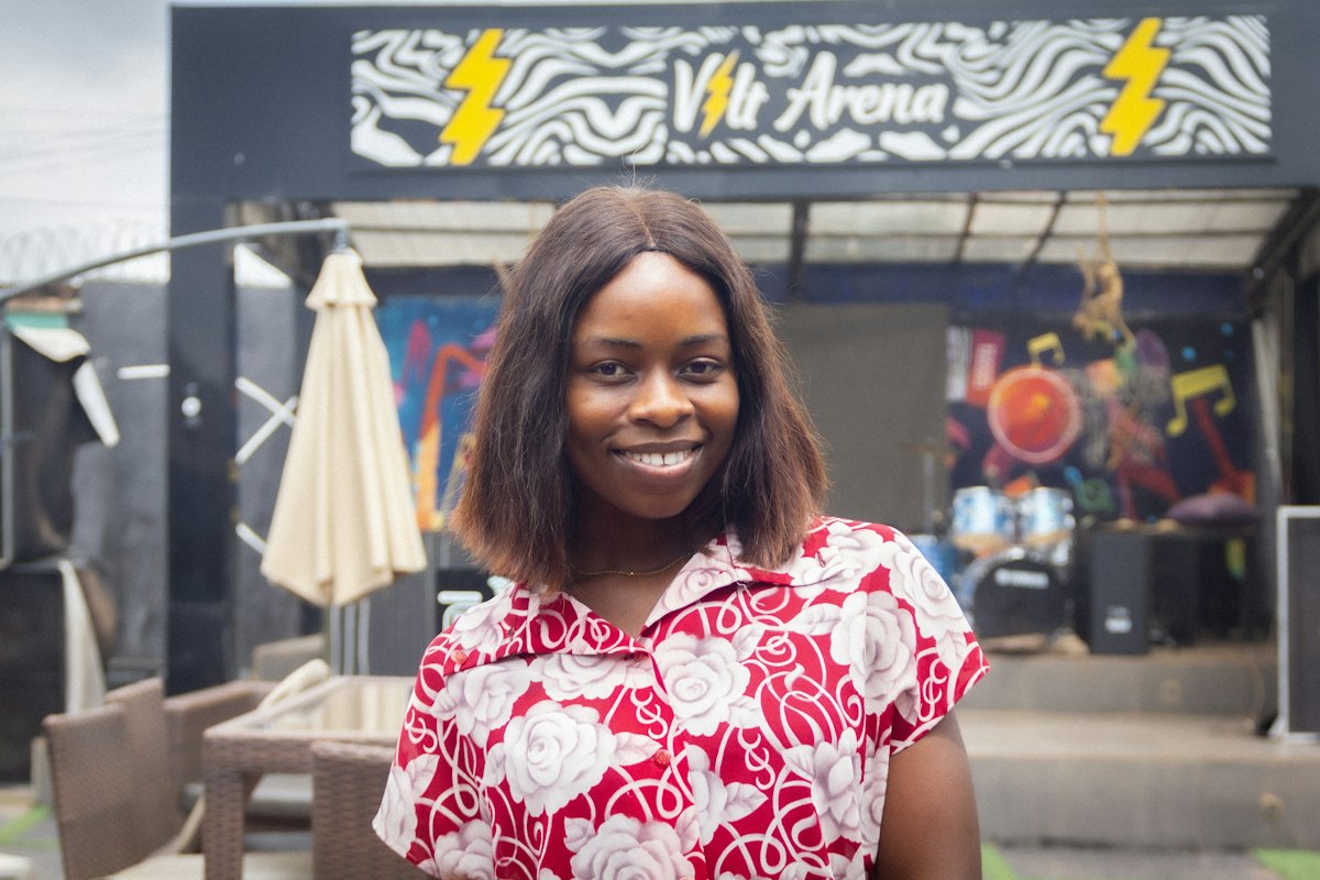 A smiling woman in a red floral top standing outside a venue in Nigeria